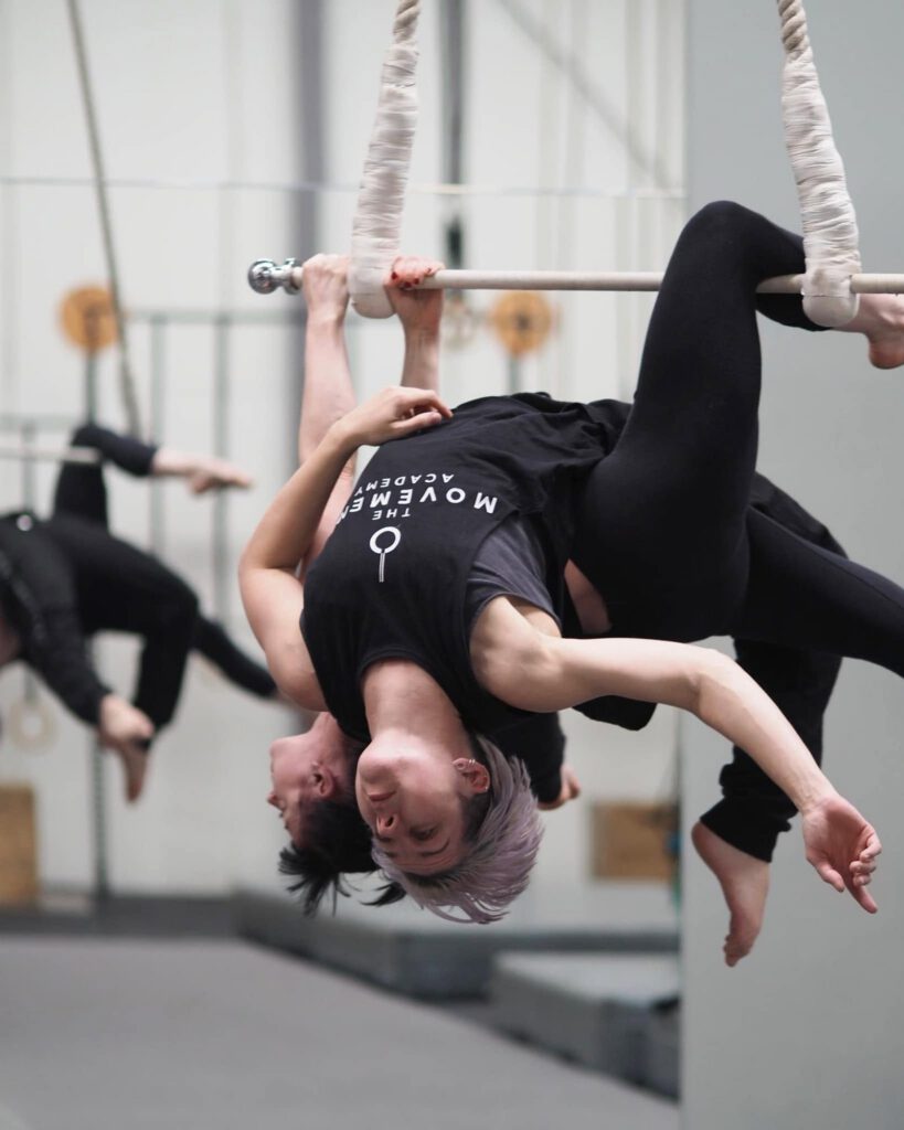 Duo Aerialists performing an inverted pose on a trapeze at The Movement Academy.